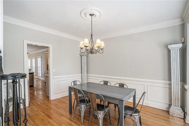 dining space featuring crown molding, a chandelier, light wood-style floors, and wainscoting