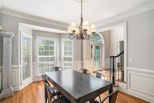 dining space featuring a chandelier, wainscoting, light wood finished floors, ornamental molding, and a decorative wall