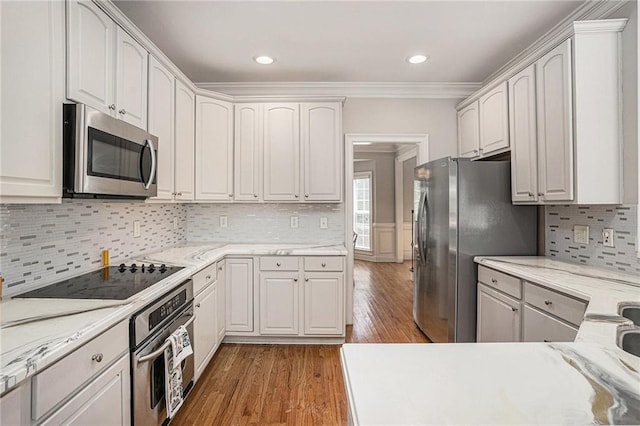 kitchen with appliances with stainless steel finishes, wood finished floors, ornamental molding, backsplash, and recessed lighting