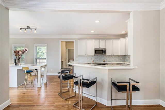 kitchen with stainless steel microwave, a breakfast bar, light wood-type flooring, decorative backsplash, and ornamental molding