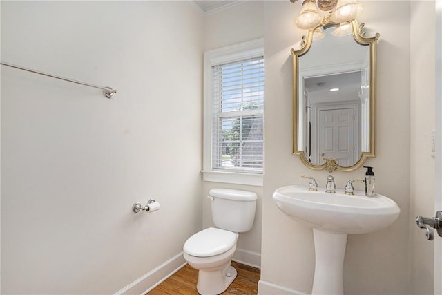 half bathroom with baseboards, toilet, wood finished floors, a chandelier, and crown molding