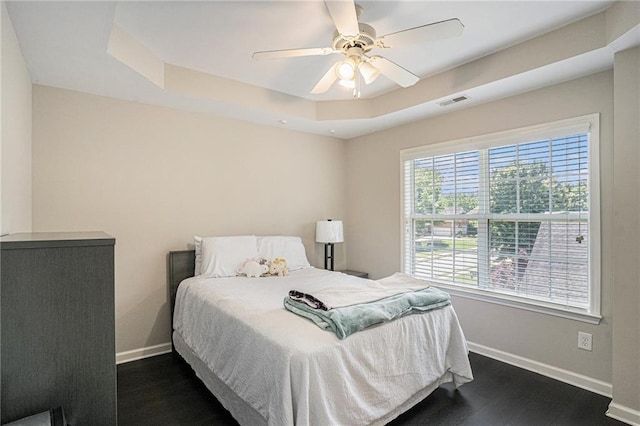 bedroom featuring baseboards, dark wood-style floors, a tray ceiling, and ceiling fan
