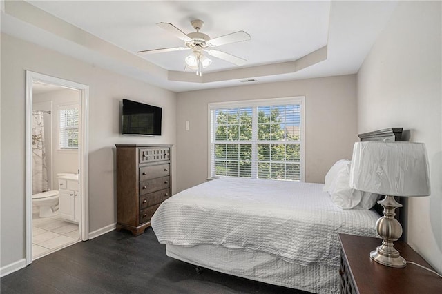 bedroom featuring dark wood-type flooring, a raised ceiling, ensuite bath, a ceiling fan, and baseboards