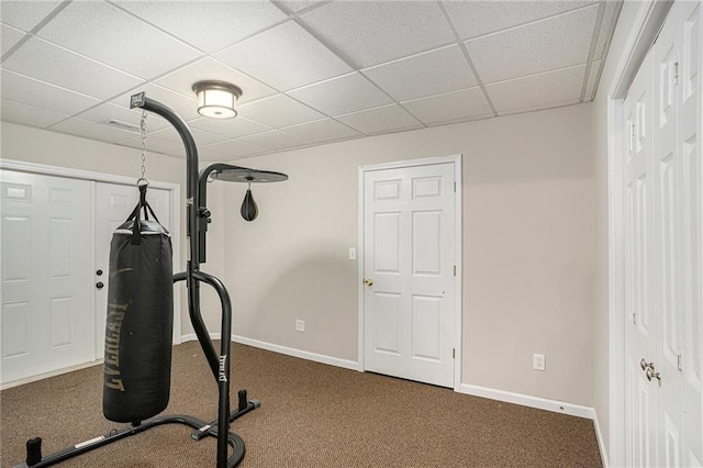 exercise area featuring a paneled ceiling, dark carpet, and baseboards