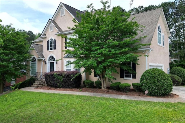 view of front of house with stucco siding, a front yard, a shingled roof, and a garage