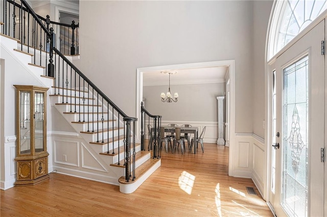 entrance foyer with wood finished floors, stairway, a towering ceiling, a chandelier, and a decorative wall