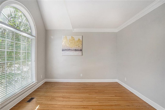 empty room with light wood-style floors, ornamental molding, baseboards, and vaulted ceiling