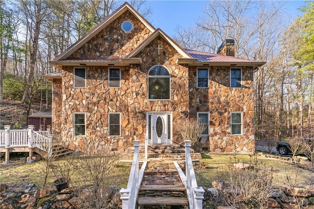 colonial home with a standing seam roof, metal roof, a chimney, and stone siding