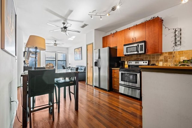 kitchen with dark wood-type flooring, appliances with stainless steel finishes, ceiling fan, and backsplash