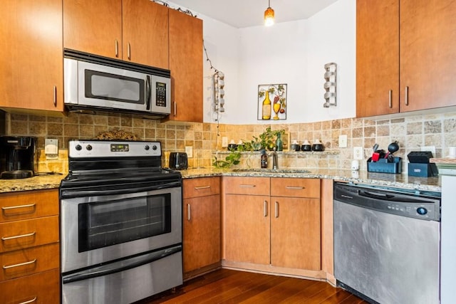 kitchen featuring stainless steel appliances, light stone countertops, dark wood-type flooring, sink, and tasteful backsplash