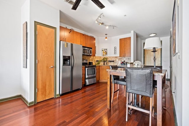 kitchen featuring kitchen peninsula, stainless steel appliances, tasteful backsplash, dark hardwood / wood-style flooring, and a breakfast bar area