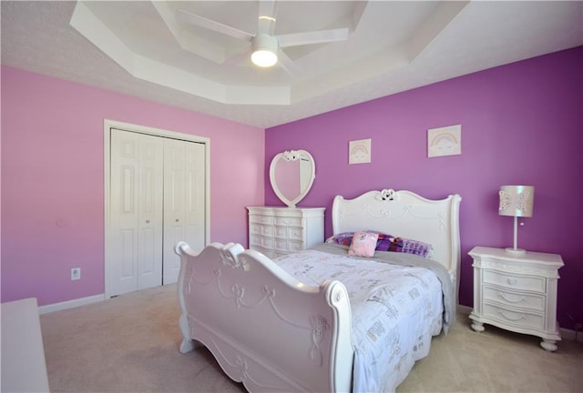 bedroom featuring baseboards, a tray ceiling, a closet, and light colored carpet