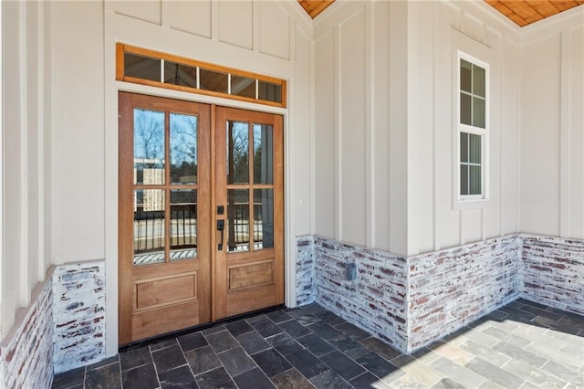 doorway to property featuring board and batten siding, french doors, and brick siding