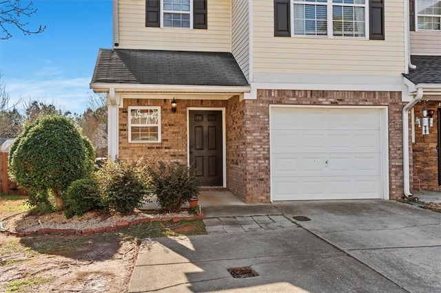 view of exterior entry with driveway, brick siding, roof with shingles, and an attached garage