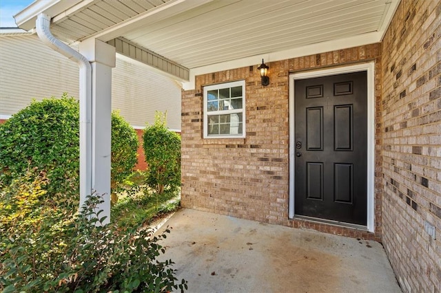 view of exterior entry with a porch and brick siding