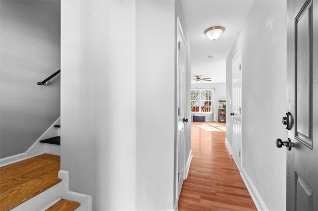 corridor featuring wood finished floors, baseboards, and stairs