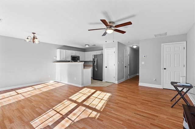 kitchen featuring light wood finished floors, visible vents, stainless steel fridge, a peninsula, and baseboards