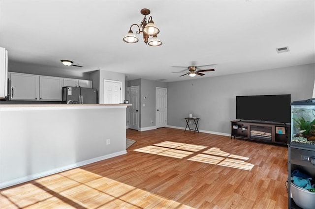 unfurnished living room featuring baseboards, ceiling fan with notable chandelier, visible vents, and light wood-style floors