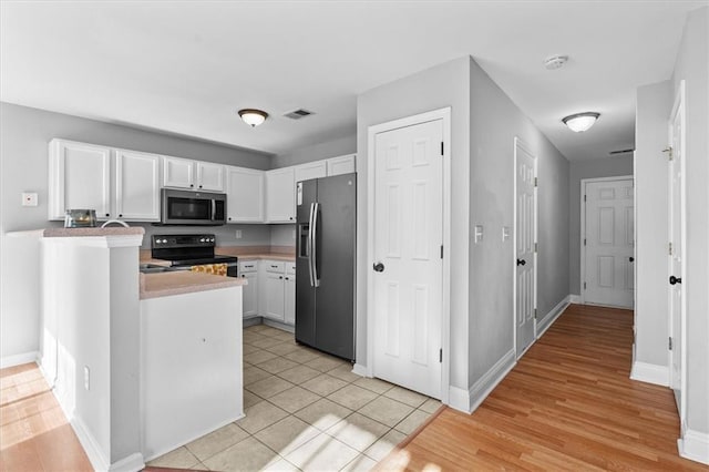 kitchen with stainless steel appliances, light countertops, white cabinetry, a peninsula, and baseboards