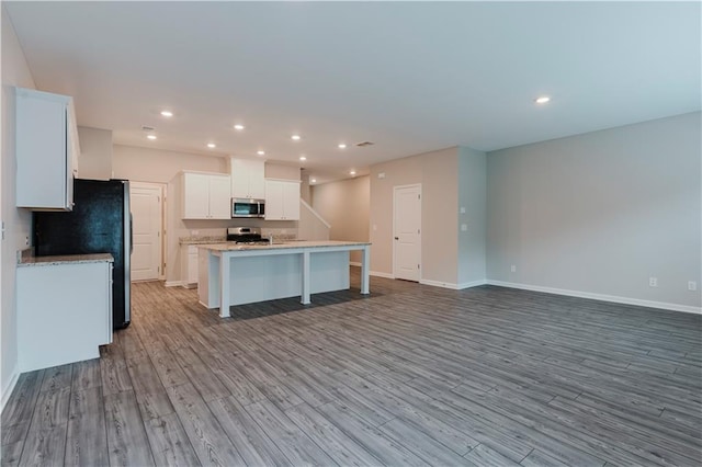 kitchen featuring stainless steel appliances, wood finished floors, a center island with sink, baseboards, and white cabinetry
