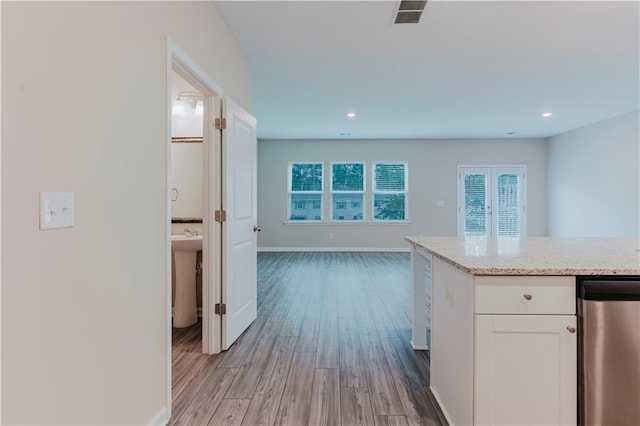 kitchen featuring white cabinets, light wood-style flooring, open floor plan, light stone counters, and baseboards