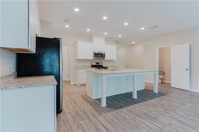kitchen featuring appliances with stainless steel finishes, light wood-type flooring, an island with sink, white cabinets, and recessed lighting