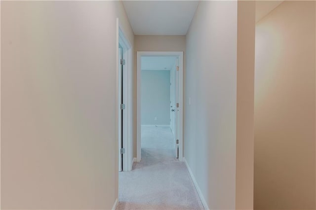 hallway featuring light carpet and baseboards