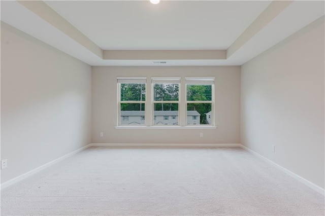 spare room featuring a raised ceiling, light carpet, and baseboards