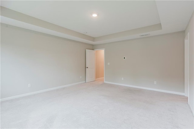 empty room featuring light colored carpet, baseboards, a raised ceiling, and recessed lighting