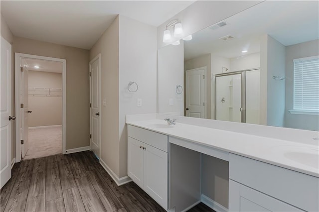 bathroom featuring a shower stall, wood finished floors, double vanity, a spacious closet, and baseboards