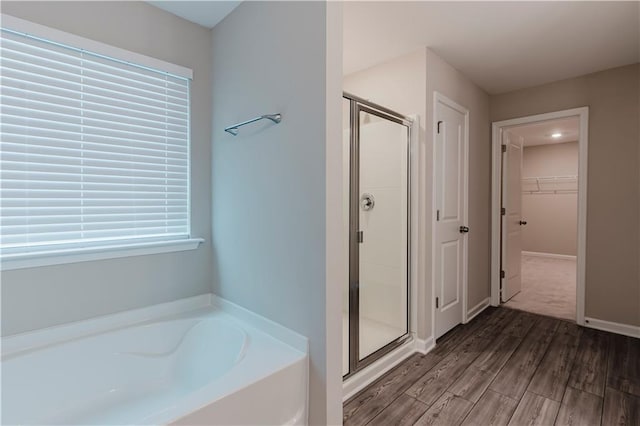 bathroom with a stall shower, a garden tub, a spacious closet, wood finished floors, and plenty of natural light