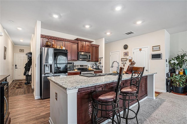 kitchen with a kitchen breakfast bar, light stone counters, dark hardwood / wood-style flooring, a kitchen island with sink, and appliances with stainless steel finishes