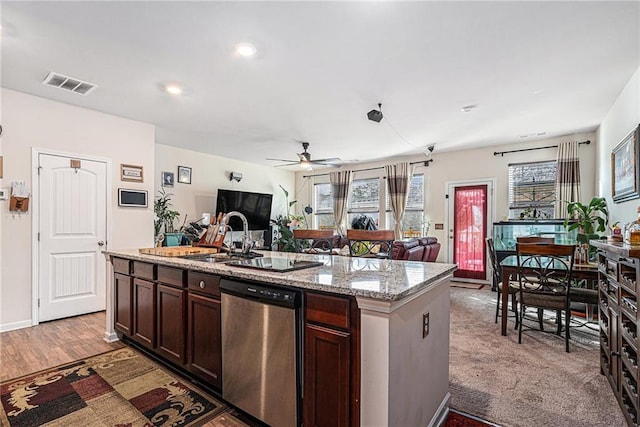 kitchen with stainless steel dishwasher, a center island with sink, light stone countertops, and a wealth of natural light