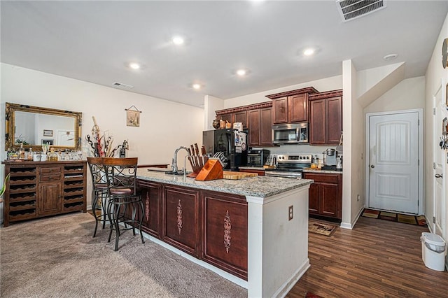 kitchen with a kitchen breakfast bar, light stone counters, stainless steel appliances, a kitchen island with sink, and sink