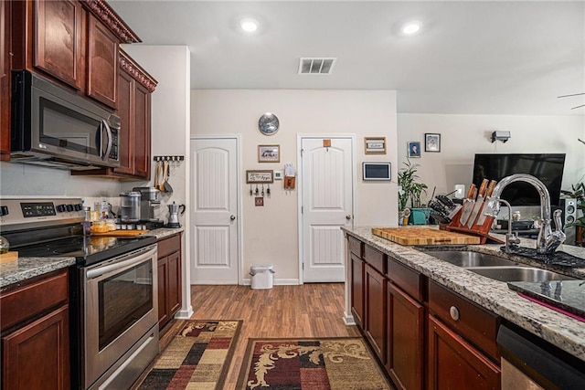 kitchen with hardwood / wood-style flooring, sink, light stone countertops, and appliances with stainless steel finishes