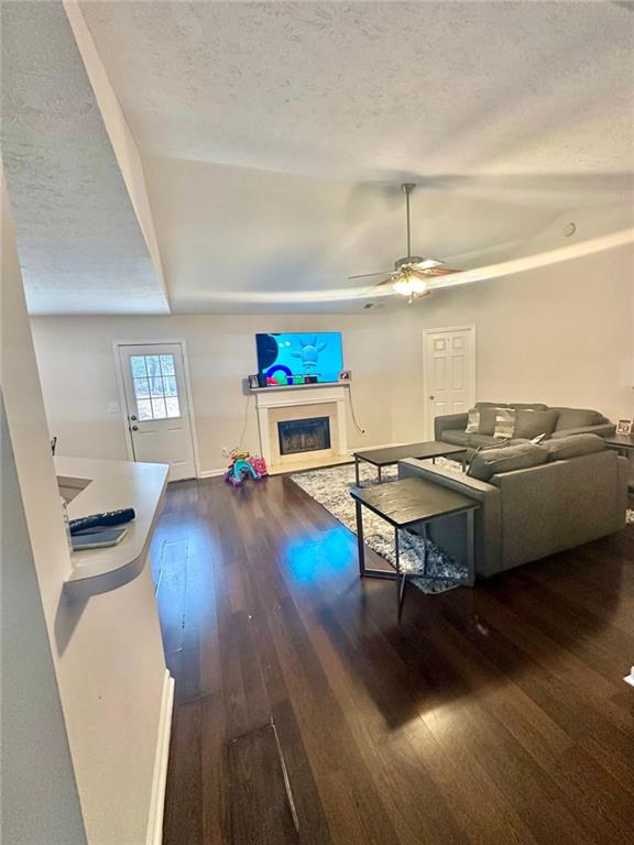 living area with a textured ceiling, baseboards, a fireplace, wood finished floors, and a ceiling fan