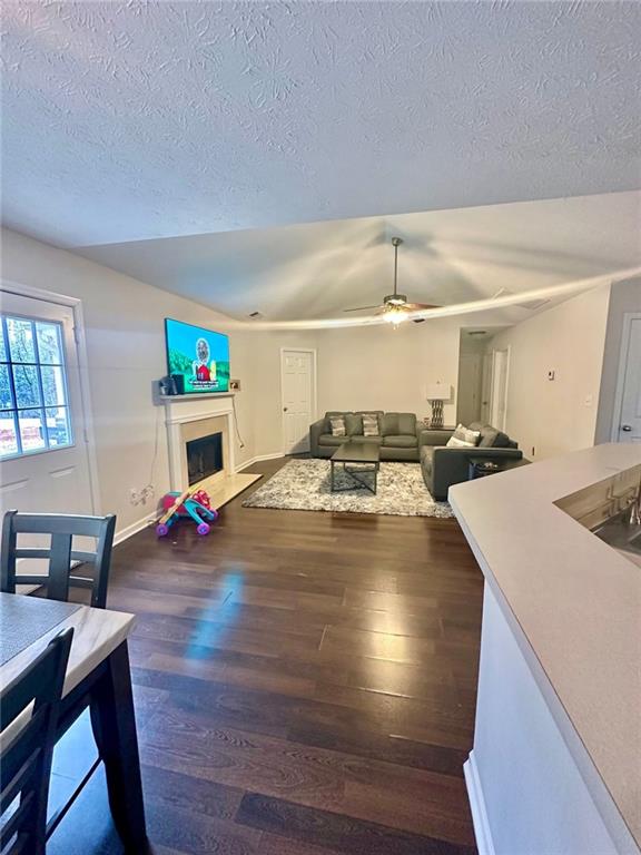 living room with a textured ceiling, baseboards, a fireplace, wood finished floors, and a ceiling fan