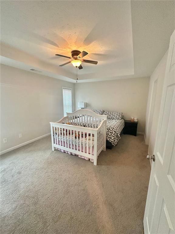 carpeted bedroom featuring ceiling fan, baseboards, and a tray ceiling