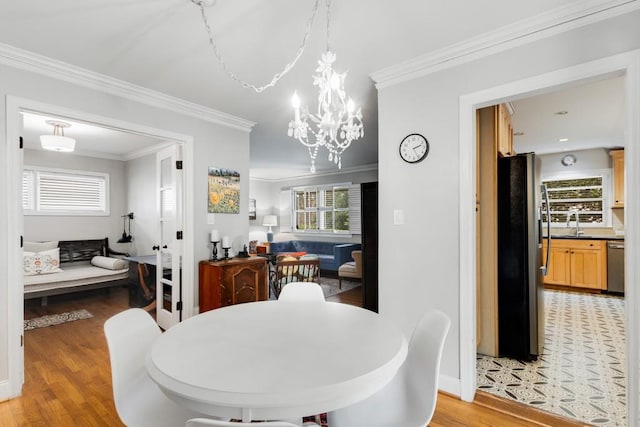 dining room featuring sink, light wood-type flooring, crown molding, and a chandelier