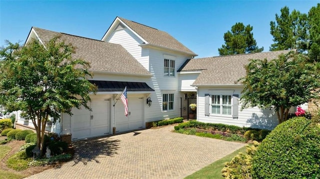 traditional-style house featuring decorative driveway, a shingled roof, and a garage
