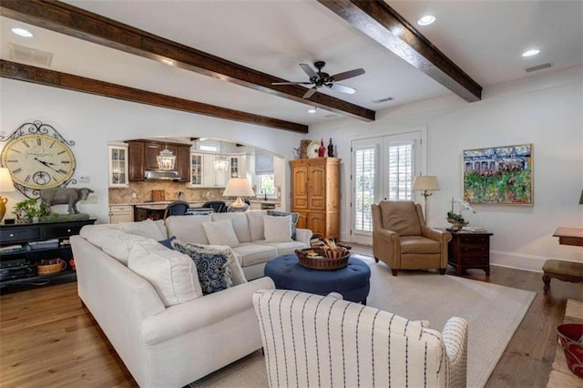 living room featuring light wood-type flooring, ceiling fan, arched walkways, beamed ceiling, and baseboards