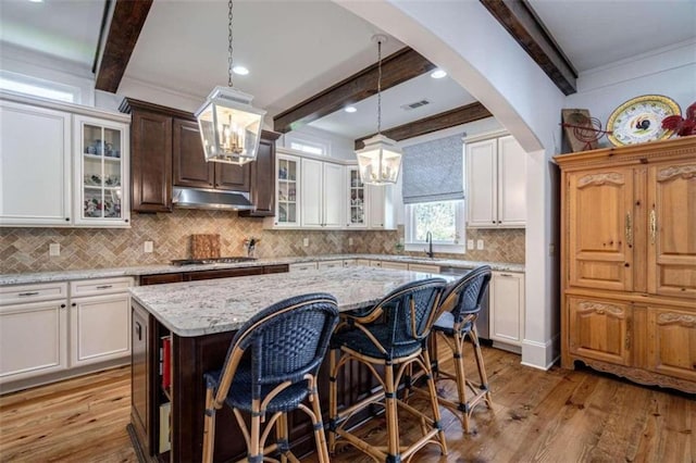 kitchen featuring a chandelier, beamed ceiling, wood-type flooring, under cabinet range hood, and tasteful backsplash