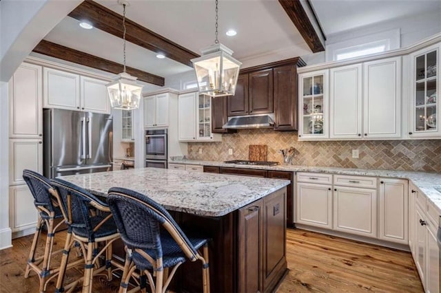kitchen featuring a chandelier, beamed ceiling, stainless steel appliances, under cabinet range hood, and a center island