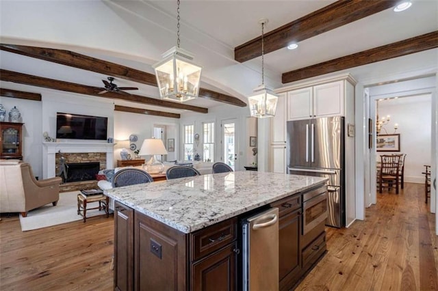 kitchen featuring a chandelier, freestanding refrigerator, white cabinets, beam ceiling, and a stone fireplace
