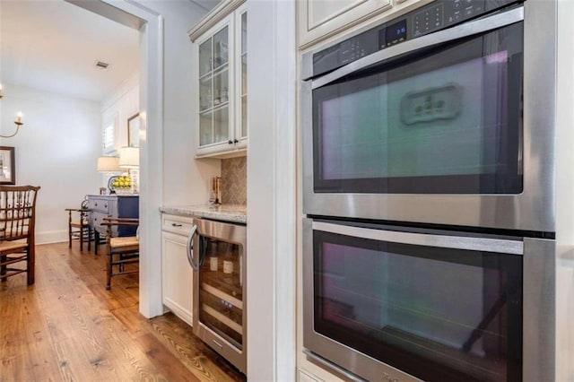 bar area featuring wine cooler, double oven, wood finished floors, and tasteful backsplash