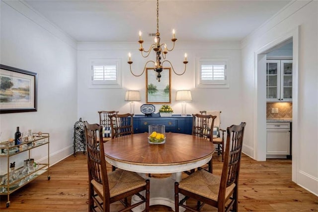 dining space with light wood-type flooring, a chandelier, ornamental molding, and baseboards