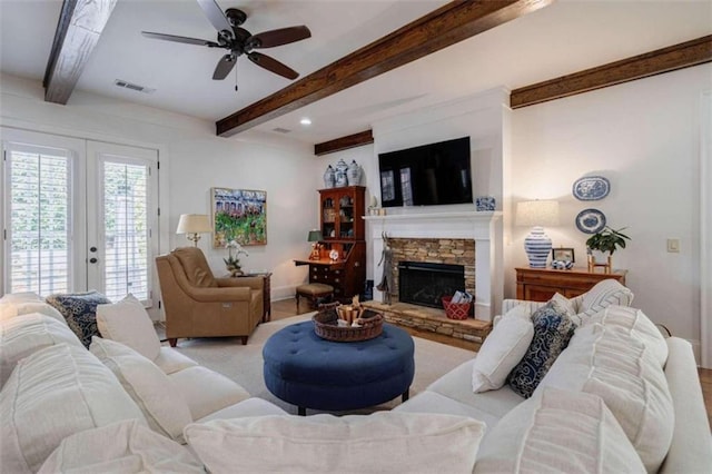 living room featuring beam ceiling, ceiling fan, a stone fireplace, baseboards, and french doors