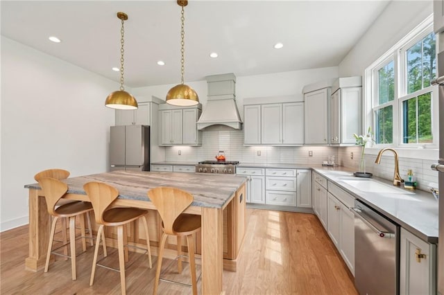 kitchen with a kitchen island, light countertops, custom range hood, a sink, and appliances with stainless steel finishes