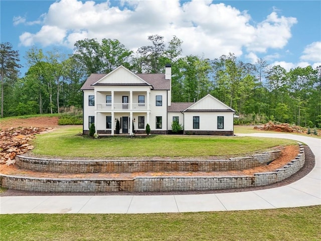 neoclassical / greek revival house featuring a front lawn, a balcony, a chimney, board and batten siding, and a porch