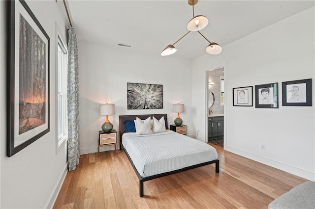 bedroom with baseboards, light wood-type flooring, ensuite bath, and visible vents